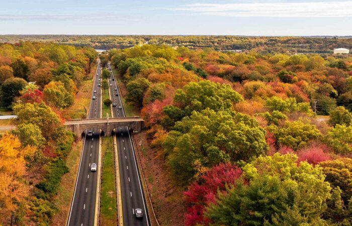 Aerial view of the Merritt Parkway and an arched stone bridge surrounded by colorful autumn trees.