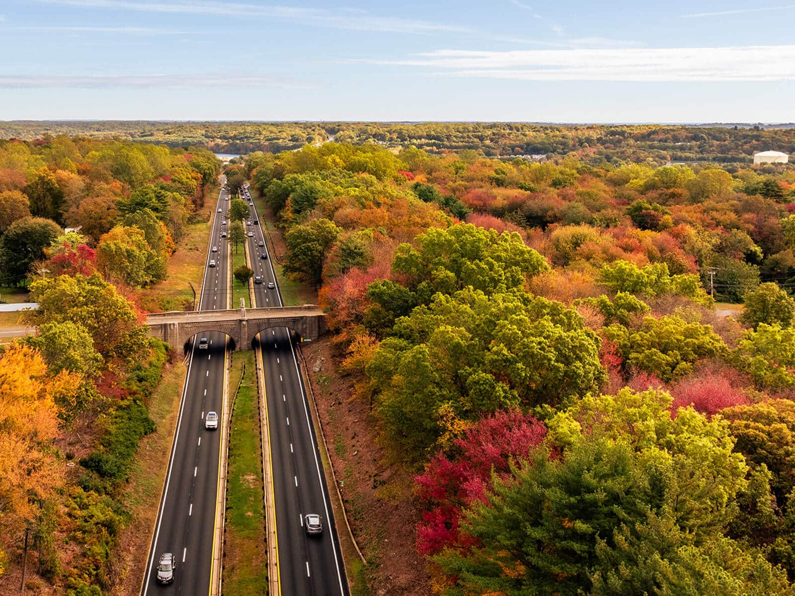 Aerial view of the Merritt Parkway and an arched stone bridge surrounded by colorful autumn trees.
